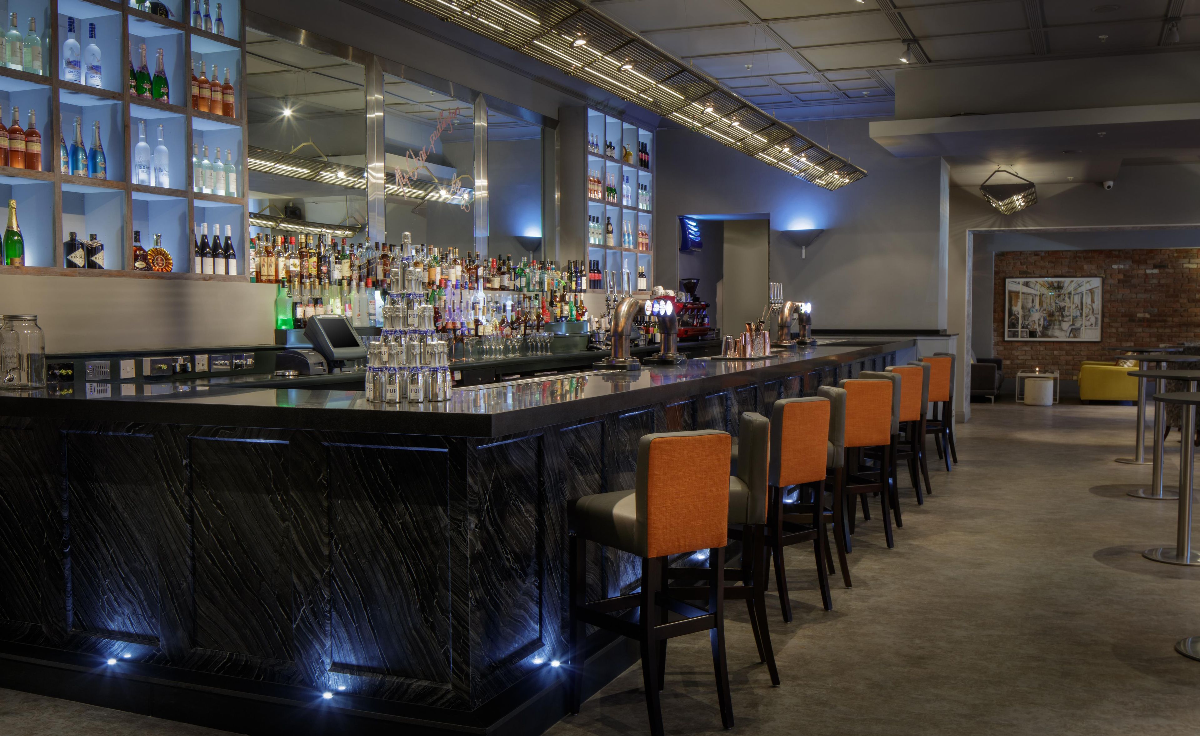 Zona de bar con encimera de mármol, varias botellas de licor y taburetes.