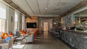 A modern bar area with seating, a brick wall, and a television. - Hilton London Paddington (London)