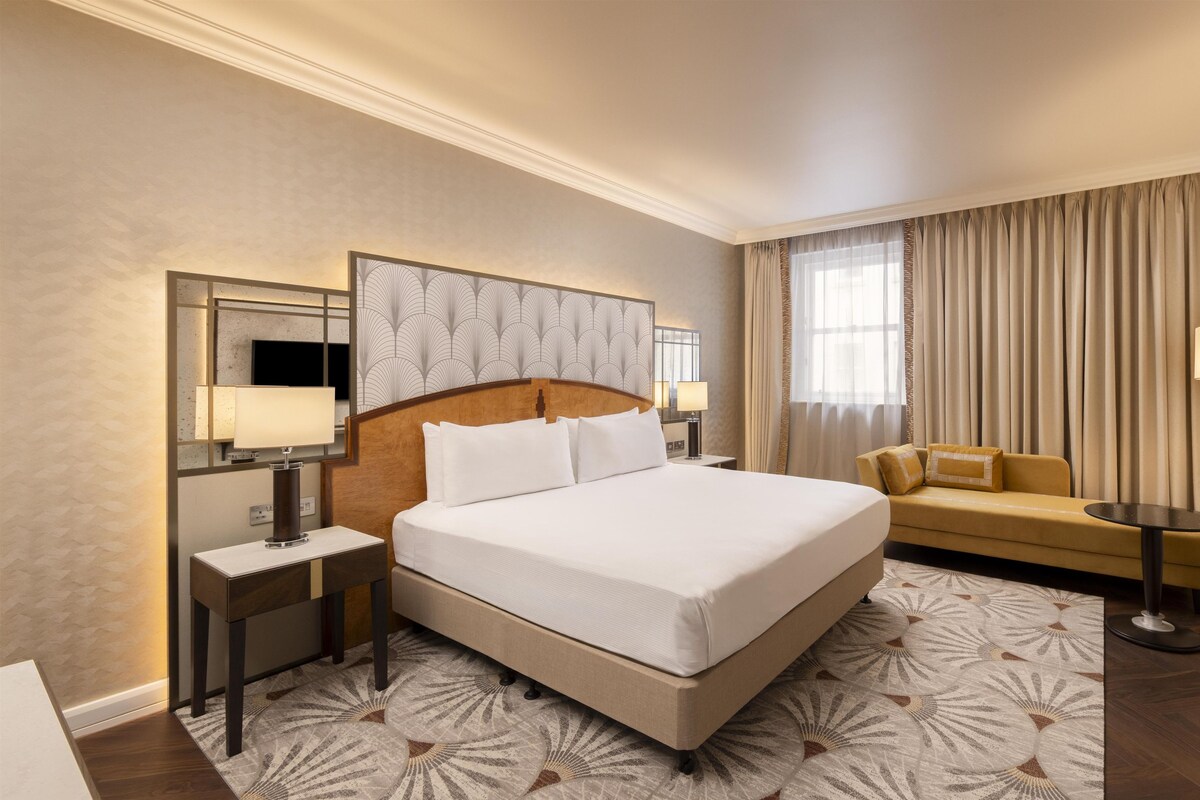 A hotel room with a large bed, a sofa, a TV, a desk, and a lamp.