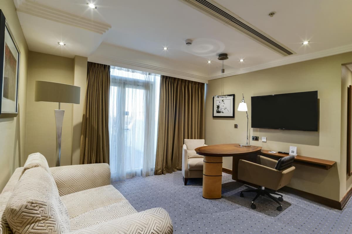 A hotel room with a sofa, a round table, a desk, a chair, a TV, and a lamp.