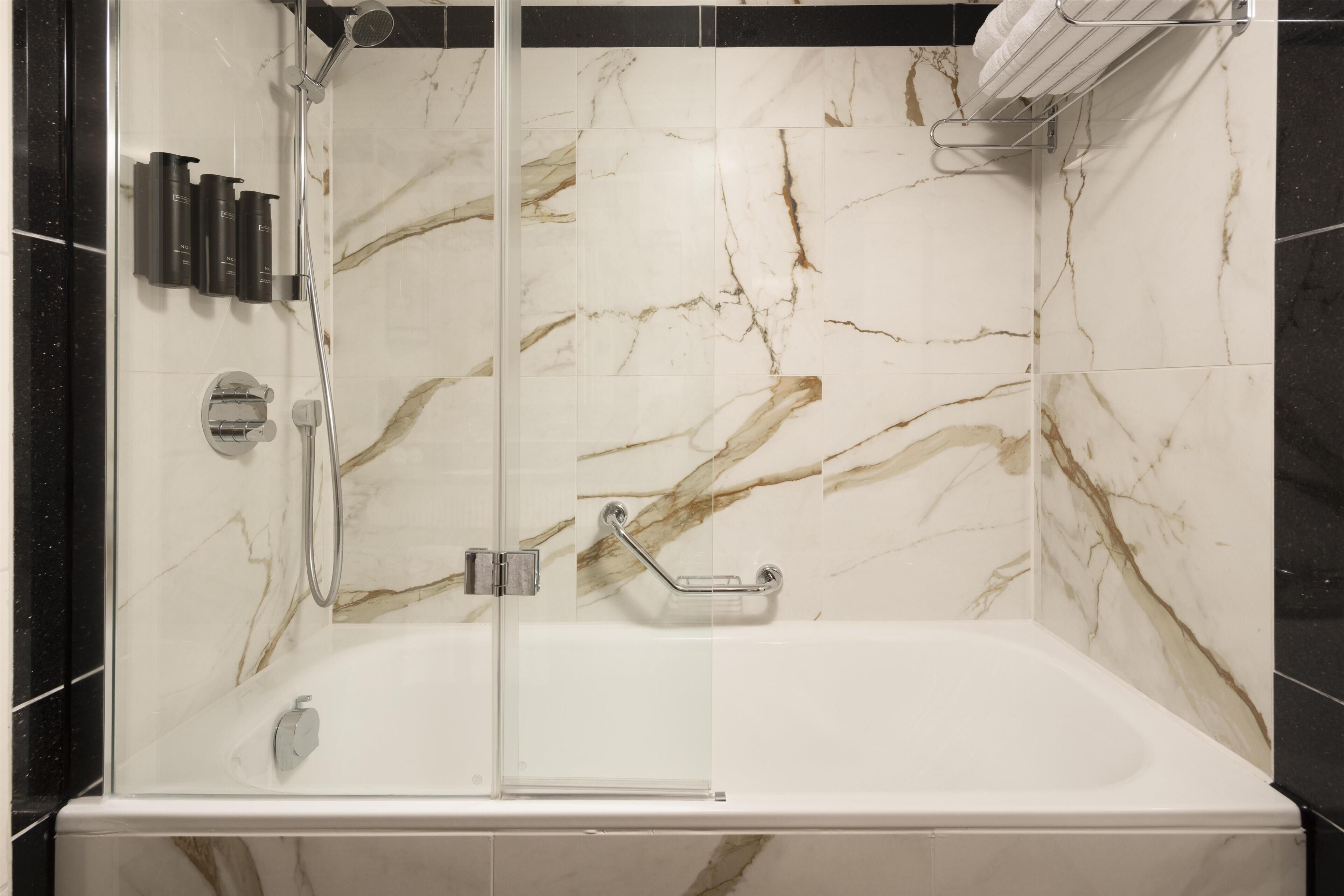 A modern bathroom with a glass-enclosed shower, a white bathtub, and marble-patterned walls.