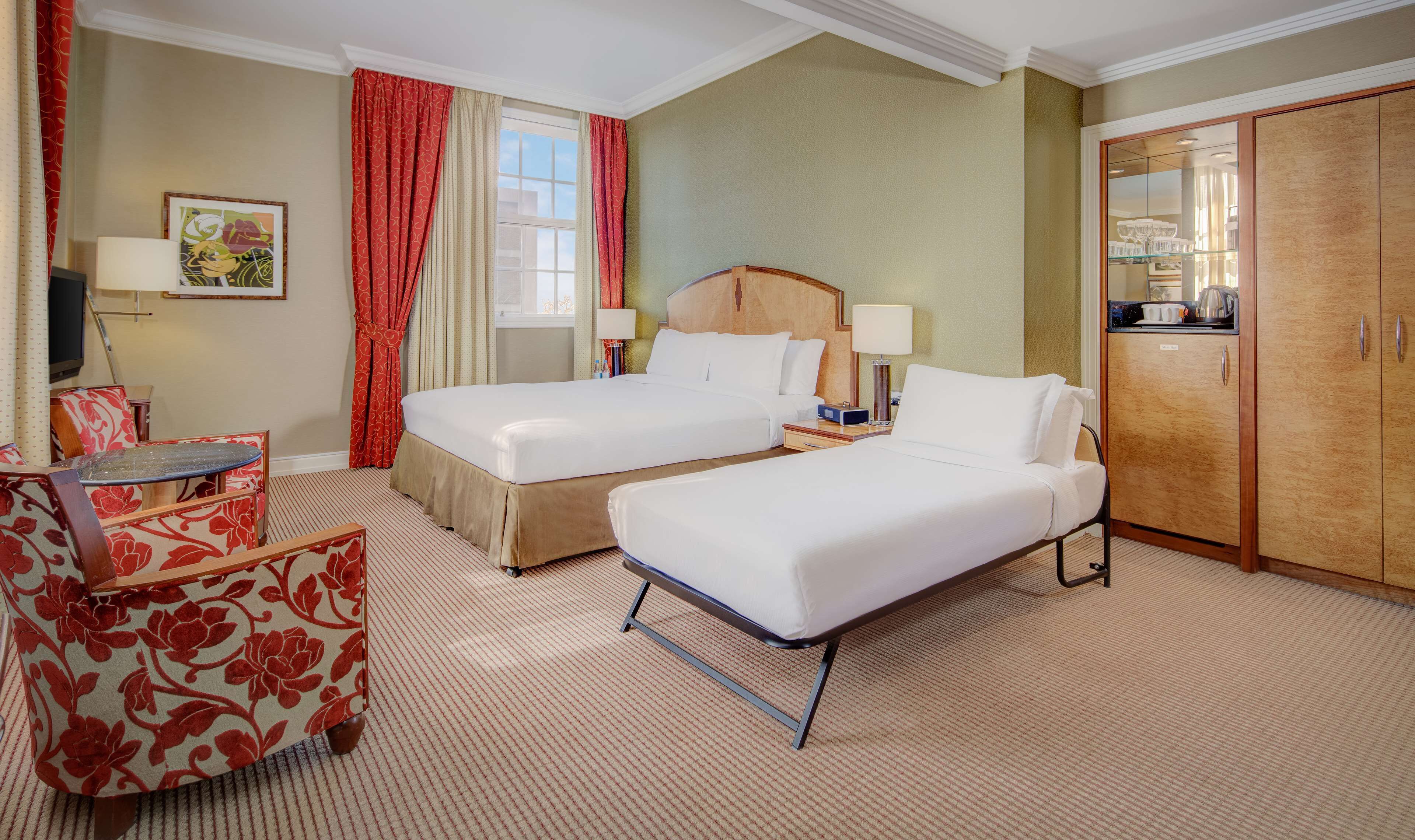 Habitación de hotel con dos camas, un escritorio, una silla y un armario.