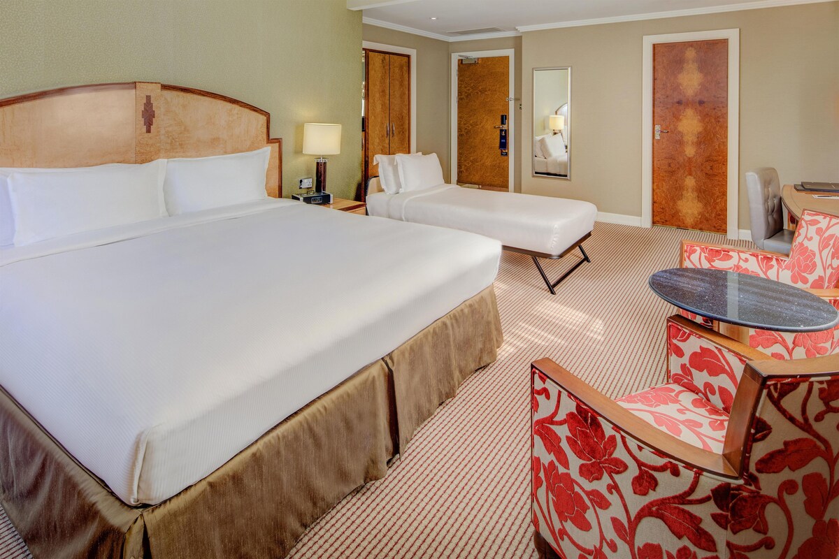 A hotel room with a large bed, two smaller beds, a desk, a chair, and a small table.