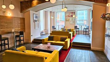 Un salon moderne avec des canapés jaunes, une moquette rouge et une vue sur la rue grâce à de grandes fenêtres.