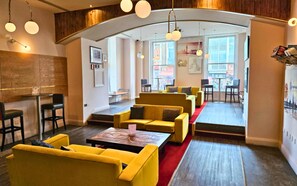 Eine moderne Lounge mit gelben Sofas, einem roten Teppich und Blick auf die Straße durch große Fenster.