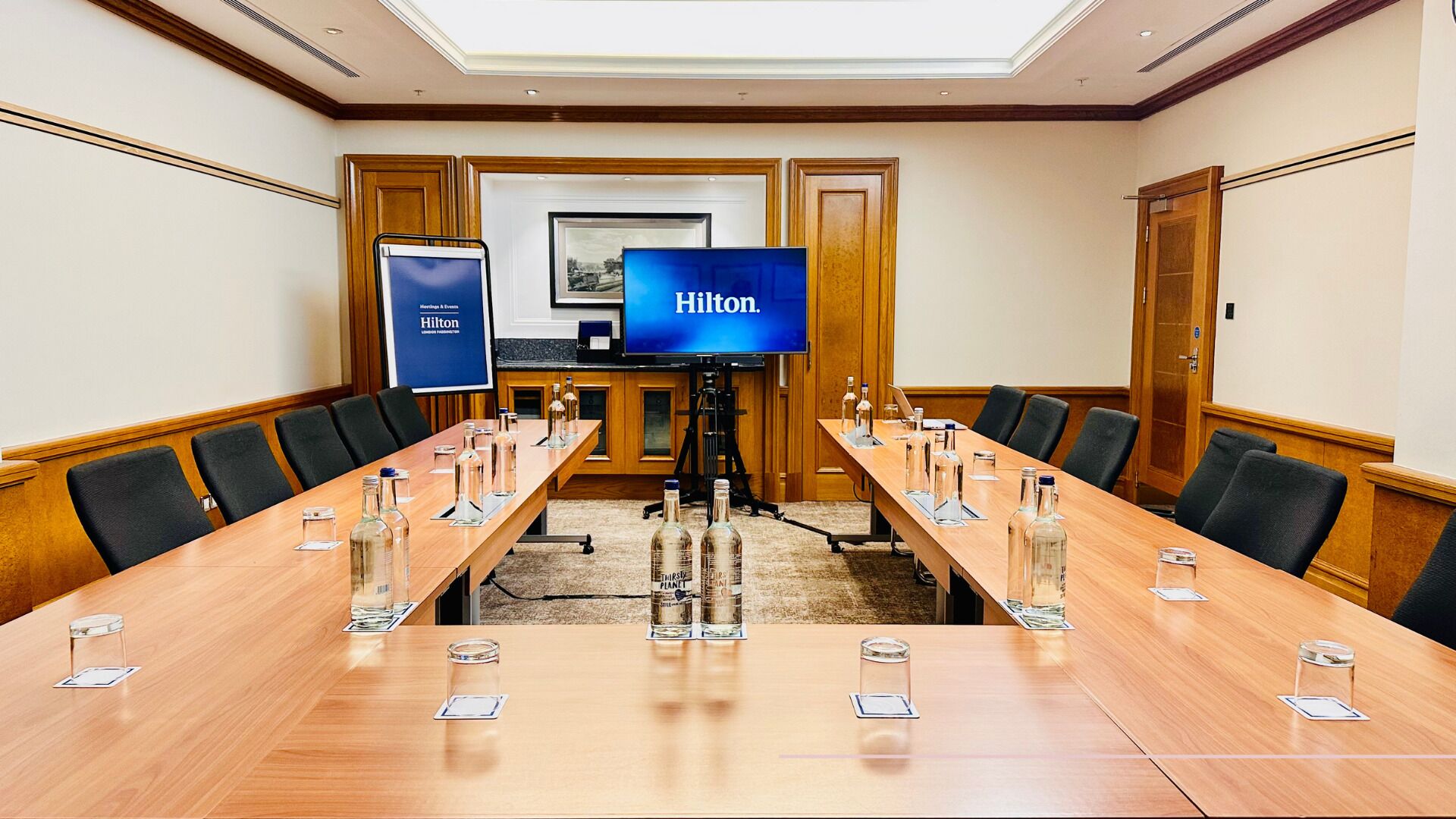 A conference room with a long table, chairs, a television screen, and a banner.