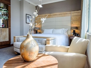 A hotel room with a bed, a sofa, a chair, a wooden coffee table, and a vase with flowers. - Hilton London Paddington (London)