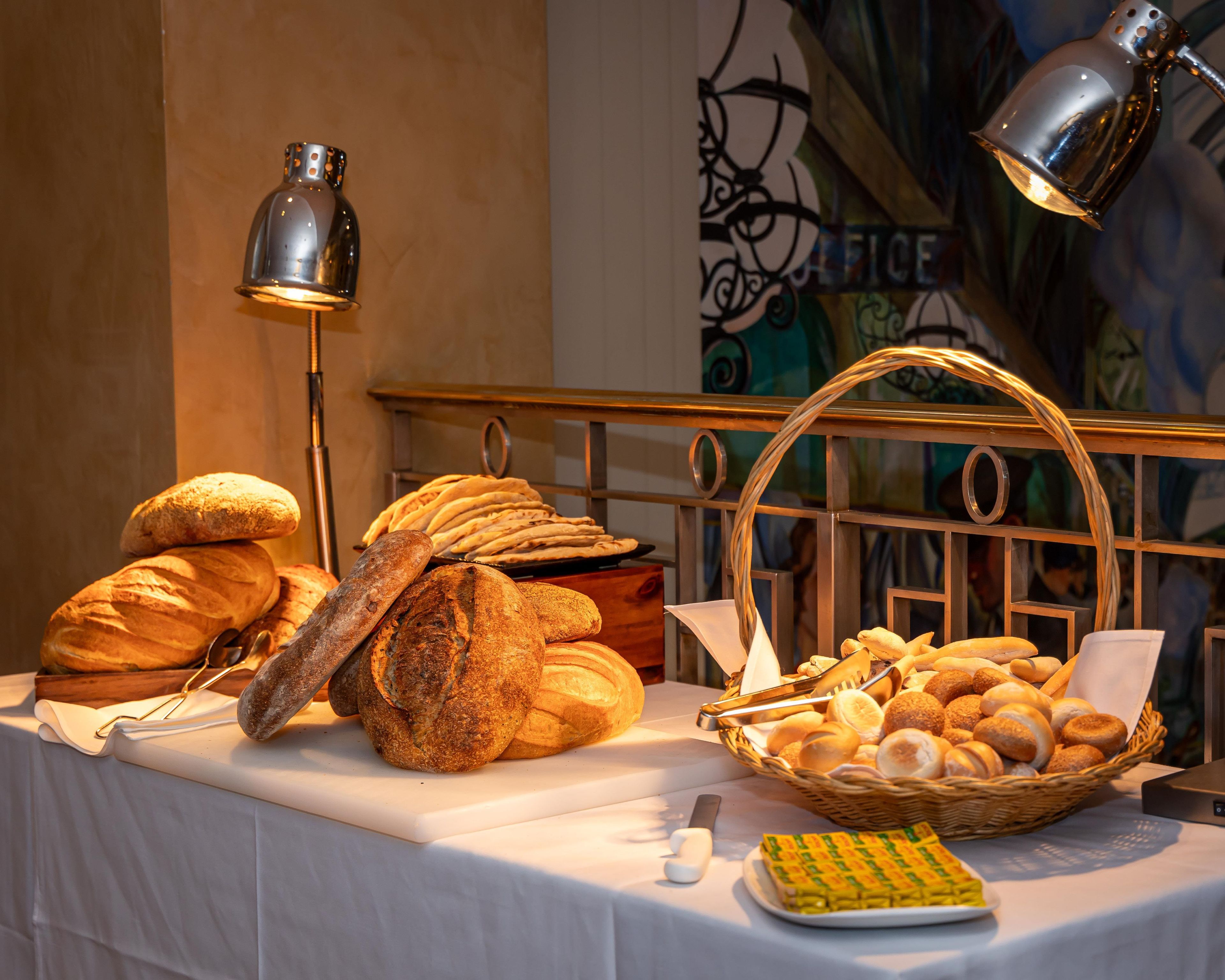 Une table sur laquelle sont disposés divers pains et pâtisseries, un panier et un couteau, le tout sur une nappe.