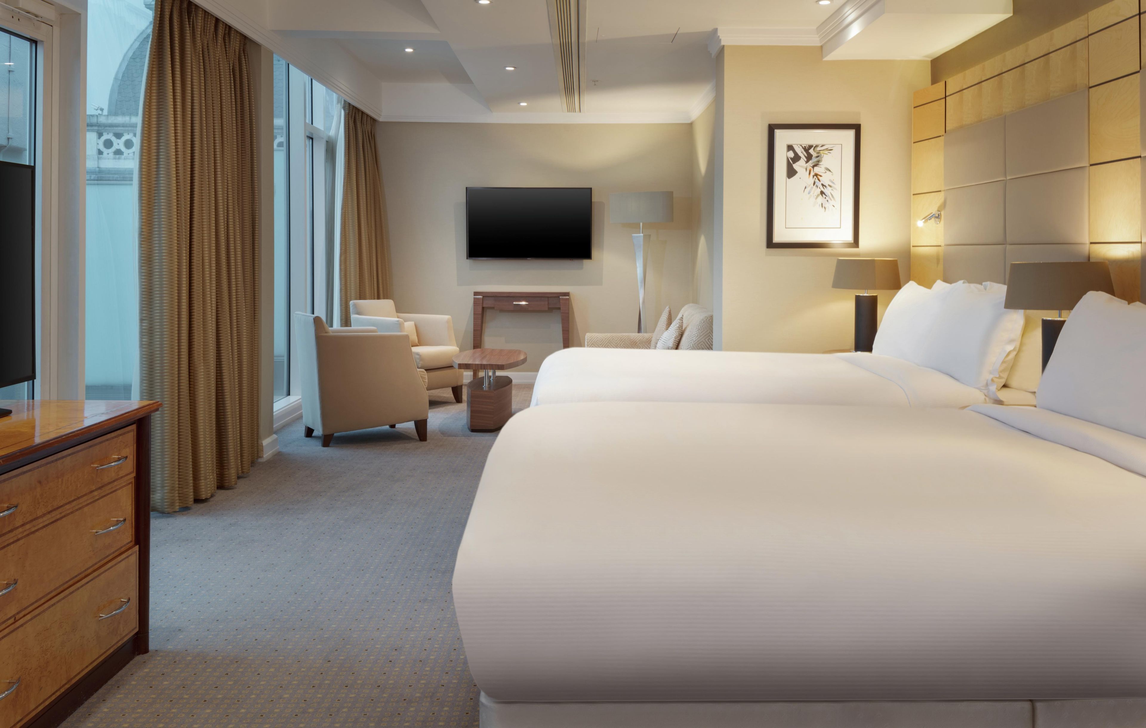 A hotel room with a large bed, a desk, a chair, a TV, and a lamp.