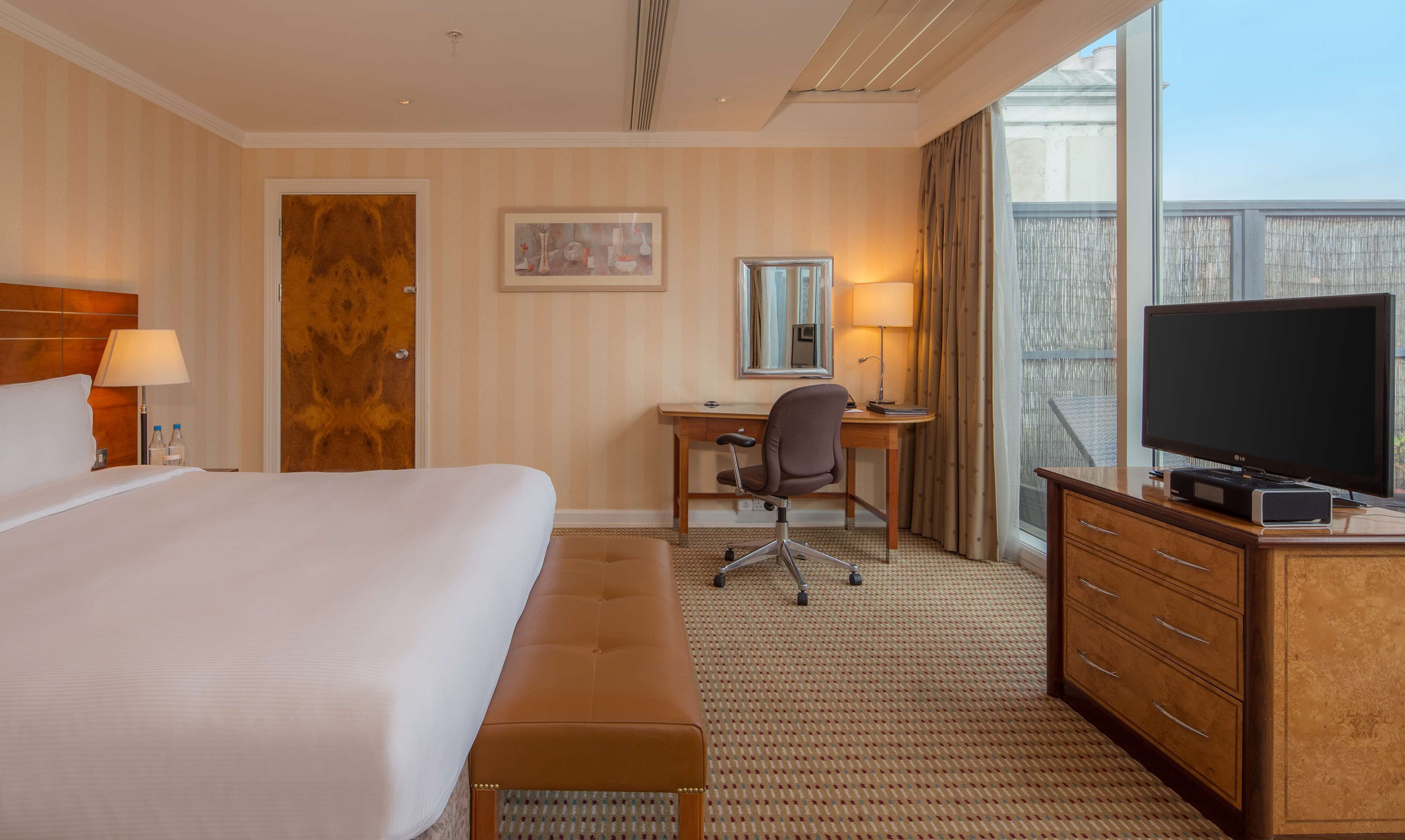 A hotel room with a large bed, a desk with a chair, a television, and a window with curtains.