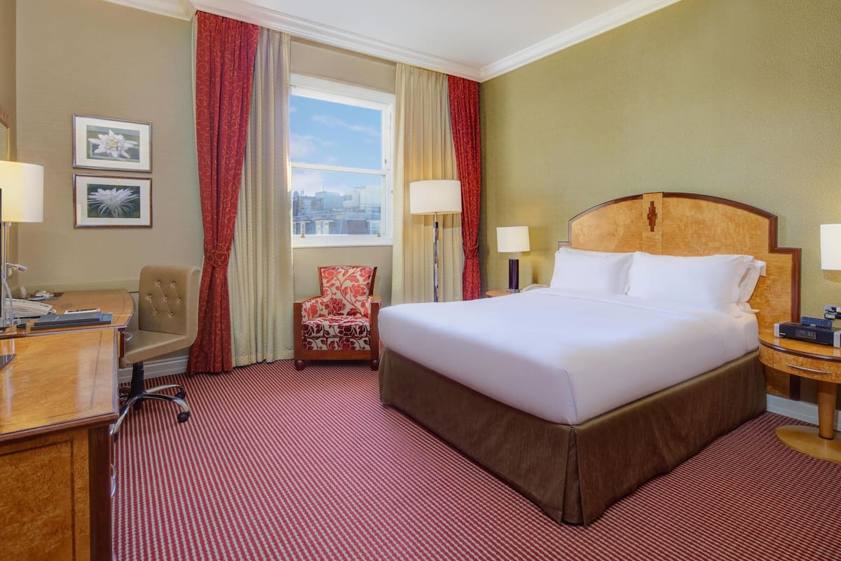 A hotel room with a large bed, a desk with a computer, a chair, a TV, and a window with curtains.