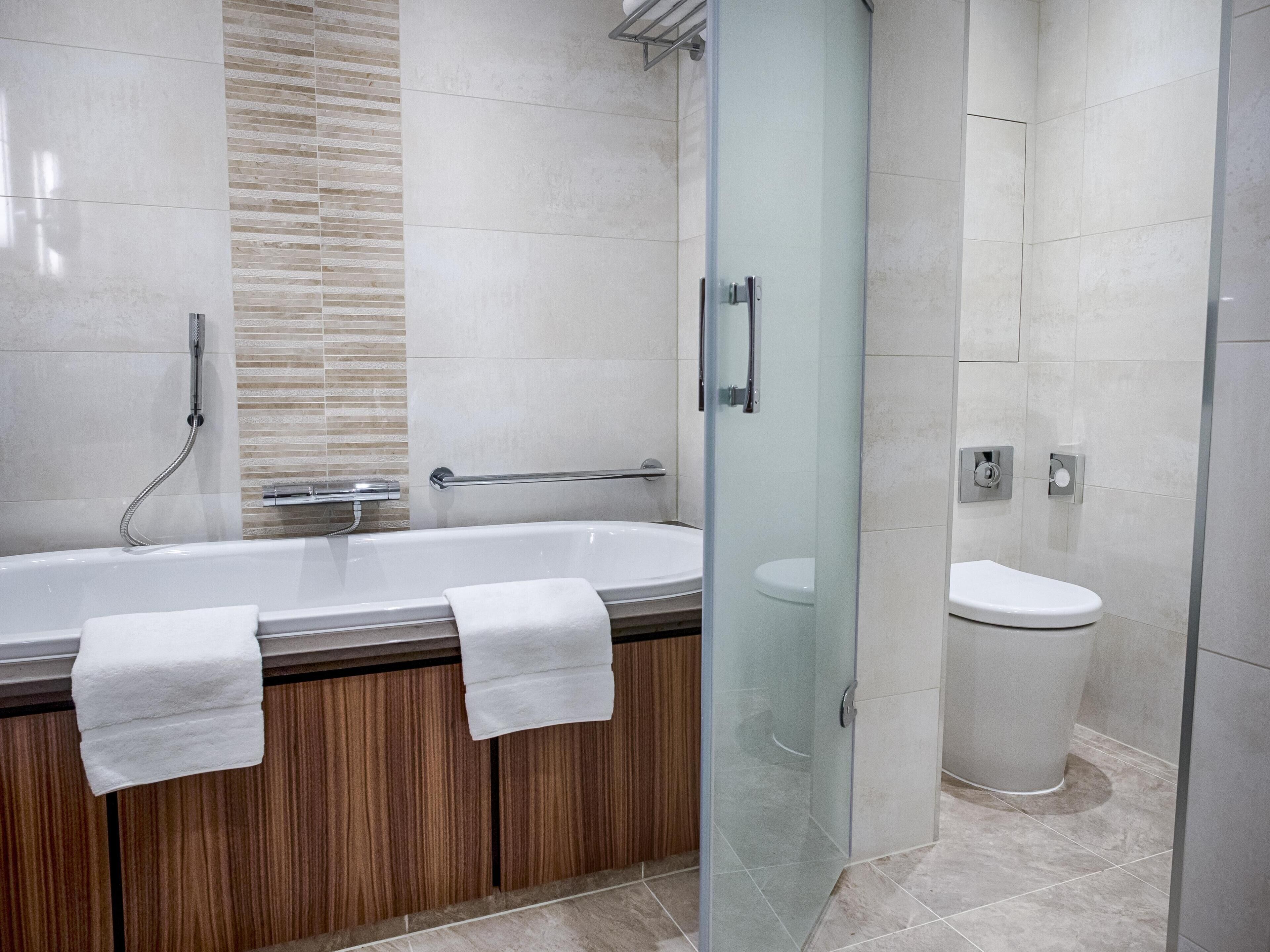 A modern bathroom with a glass-enclosed shower, a bathtub with two towels, and a toilet.