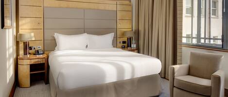 A hotel room with a large bed, two bedside tables, a chair, and a window with curtains.
