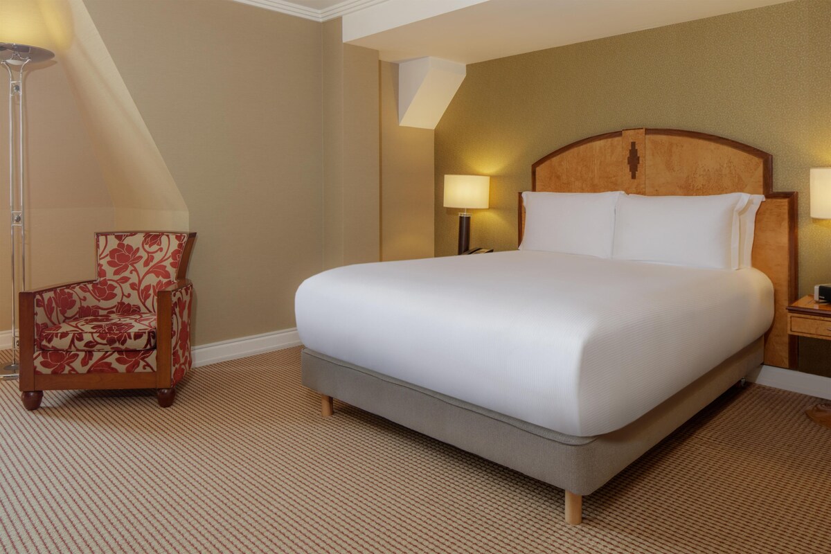 A hotel room with a large bed, a chair, a lamp, and a nightstand.