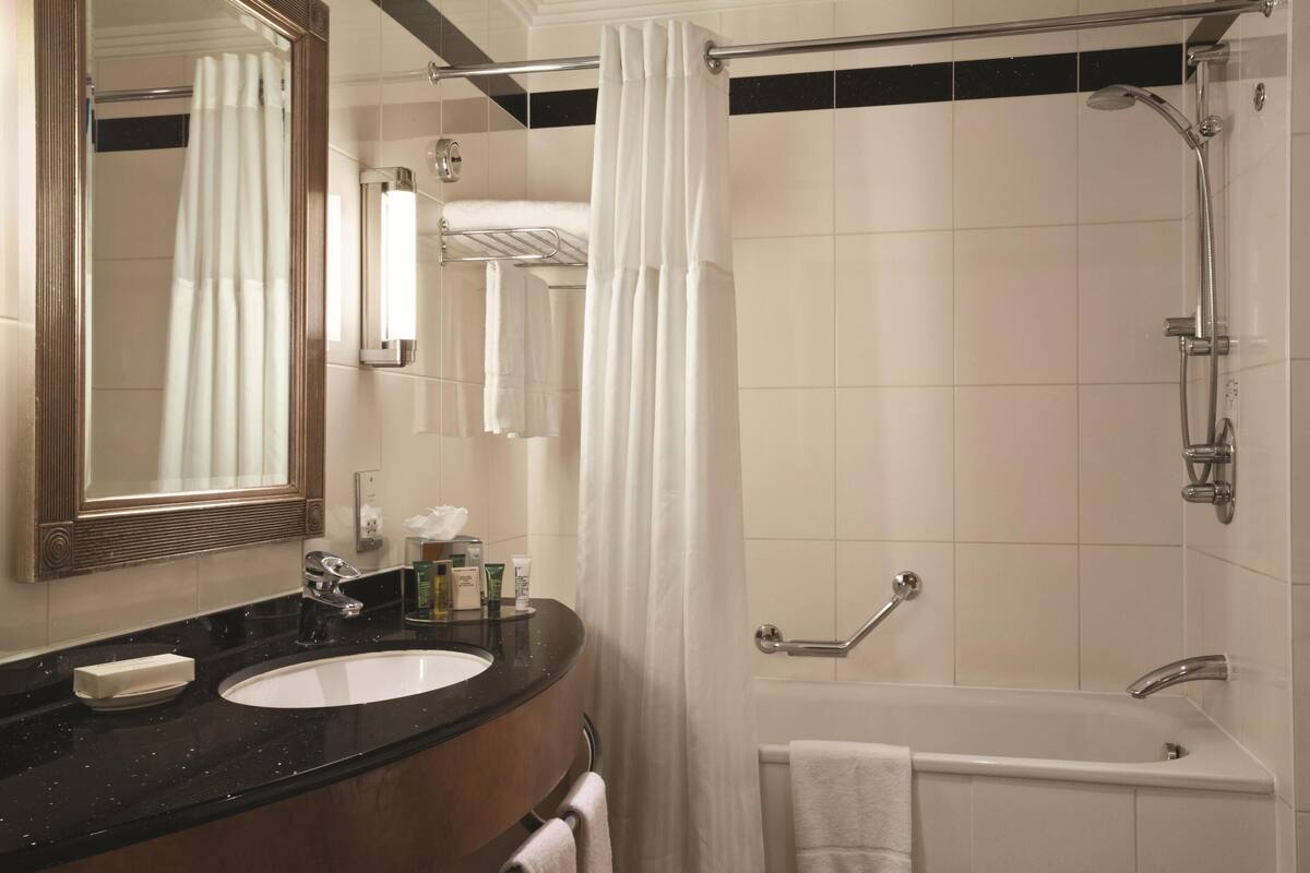 A bathroom with a sink, mirror, shower, and towel rack.