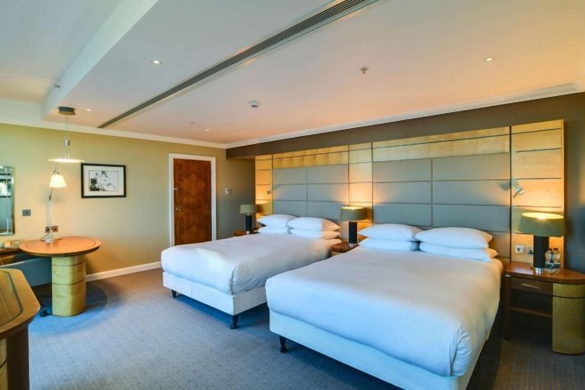 Habitación de hotel con dos camas, una mesita de noche, una lámpara y una pequeña mesa redonda.
