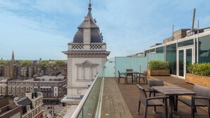 A rooftop terrace with outdoor seating, overlooking a cityscape with historic buildings. - Hilton London Paddington (London)