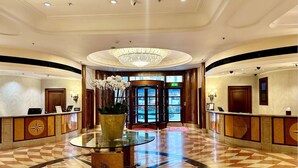 A hotel lobby with a central glass table, a chandelier, and a reception desk. - Hilton London Paddington (London)