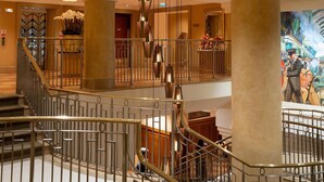 A hotel lobby with a grand staircase, large columns, and a mural on the wall. - Hilton London Paddington (London)
