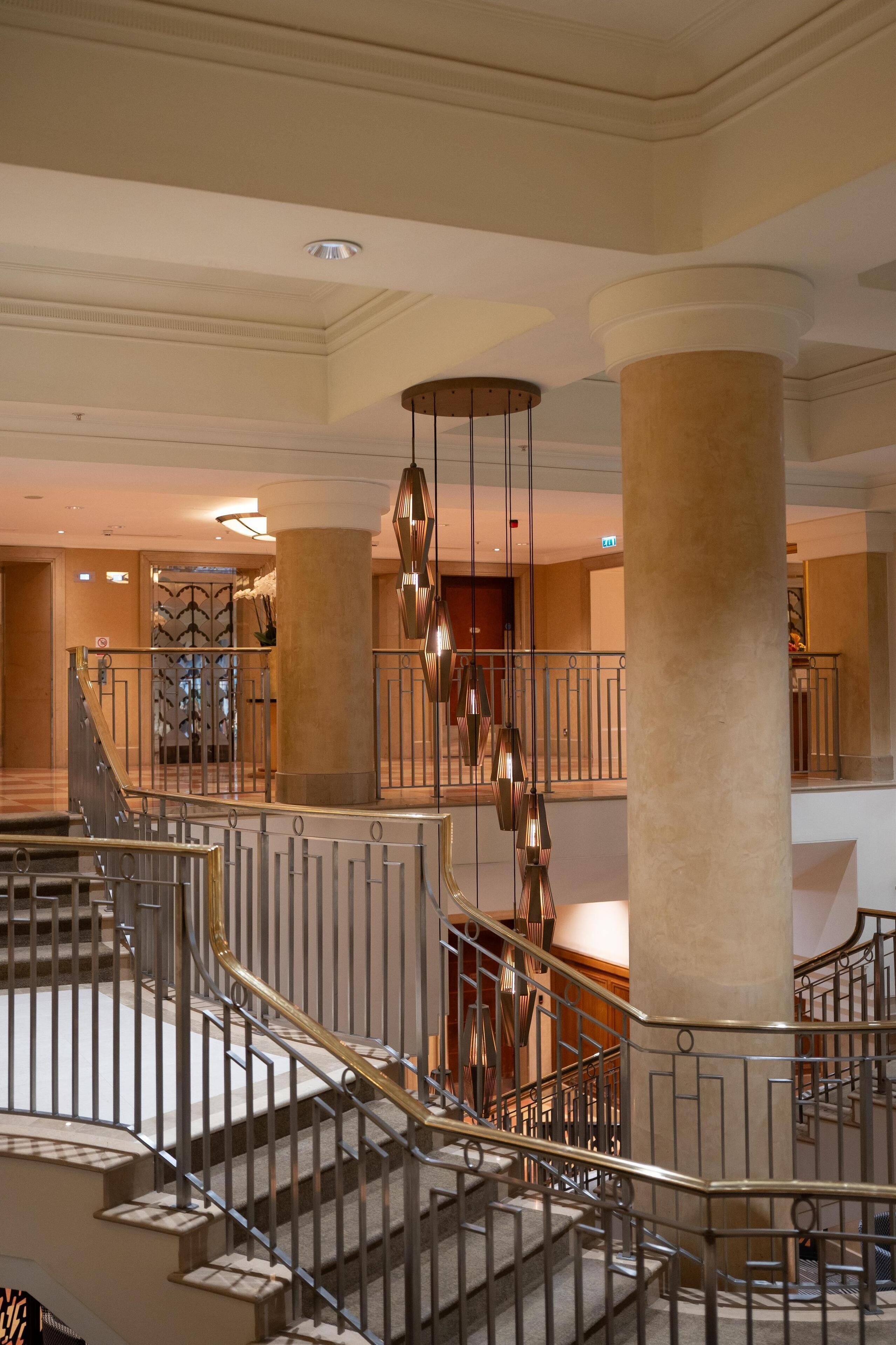 A grand hotel lobby with a central staircase, large columns, and modern lighting fixtures.