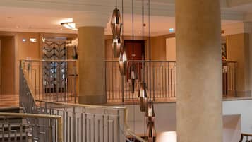 A grand hotel lobby with a central staircase, large columns, and modern lighting fixtures.