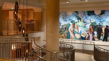 Un vestíbulo de hotel con una escalera monumental, un mural y una araña.