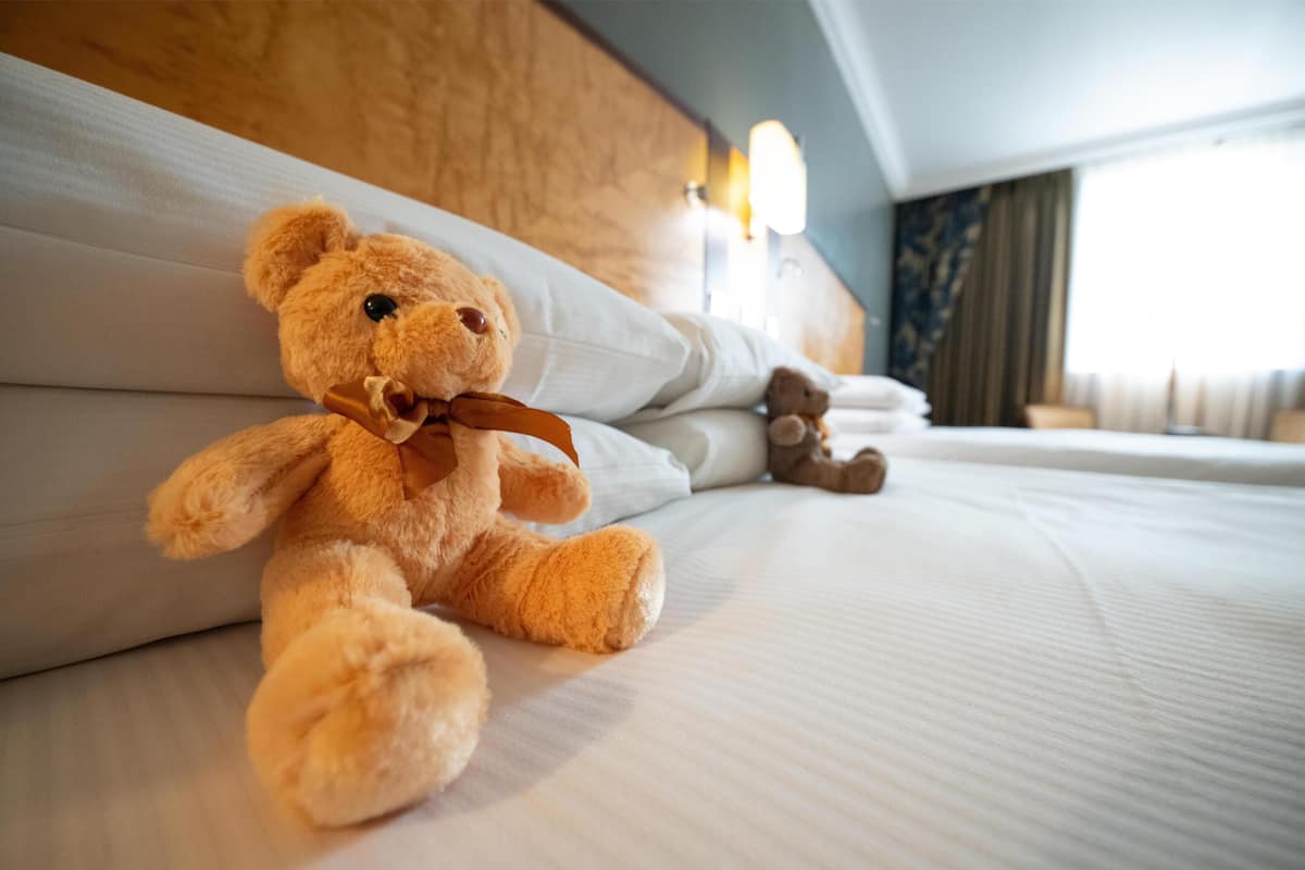A plush teddy bear on a neatly made bed with pillows and a small bedside table.