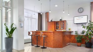 A reception area with a wooden counter, three bar stools, a clock, and a TV displaying "TRIP INN HOTELS". - Trip Inn Hotel Minerva (Frankfurt)
