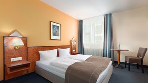 A hotel room with a bed, a desk, a chair, a lamp, a painting, and a window with curtains. - Trip Inn Hotel Minerva (Frankfurt)
