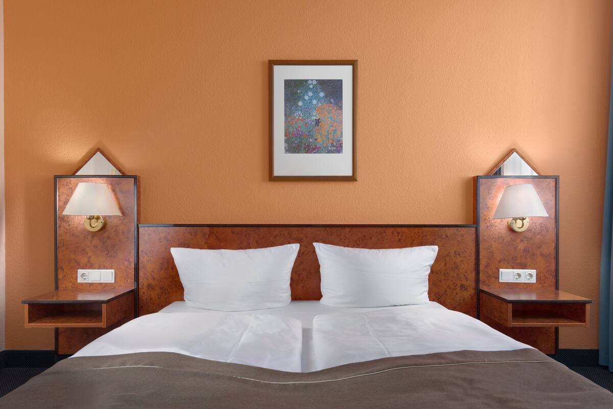 A hotel room with a large bed, two nightstands, a framed artwork on the wall, and a lamp on each nightstand.