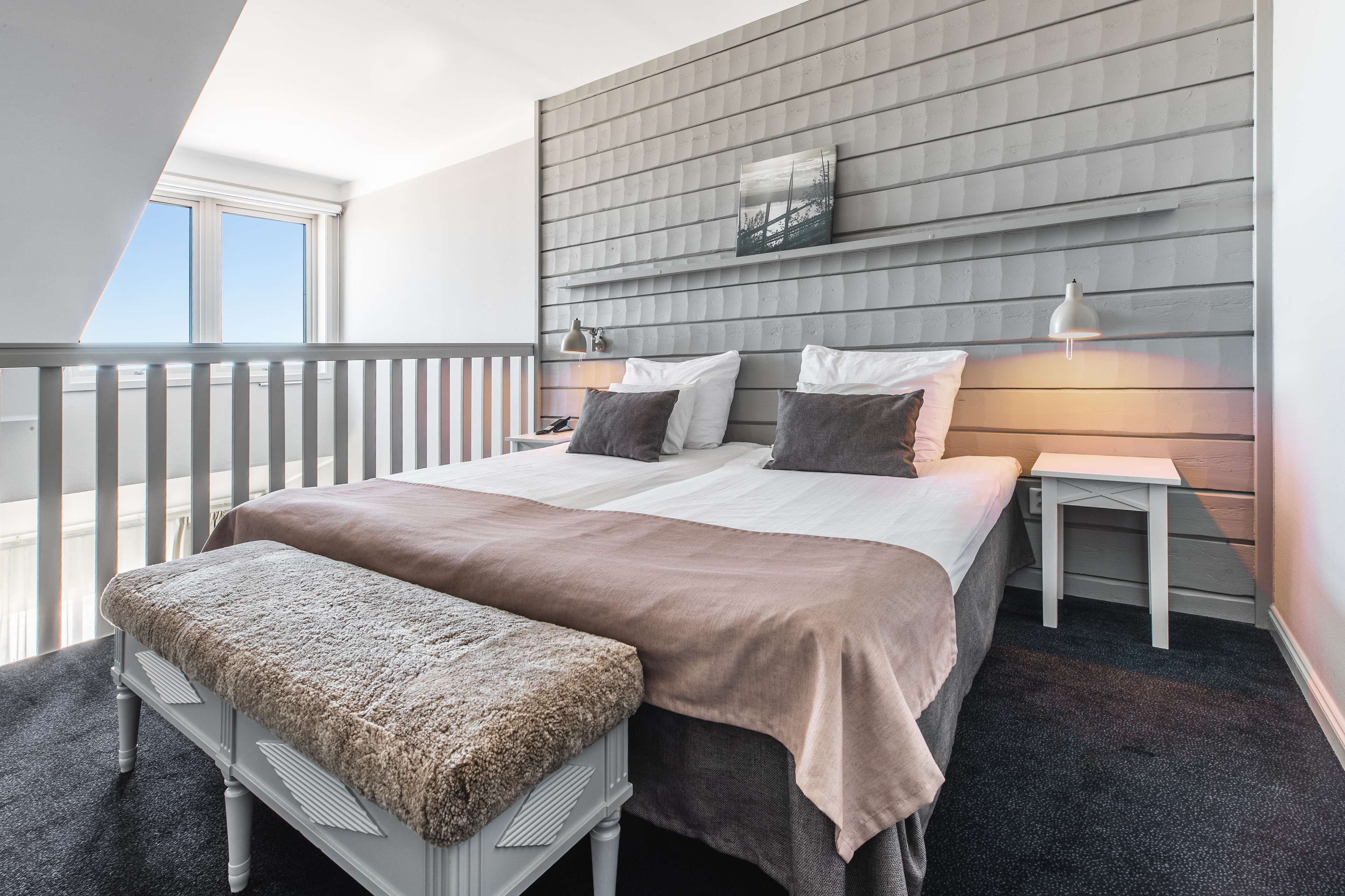 A modern bedroom with a large bed, a bench, a nightstand, and a wall-mounted lamp.