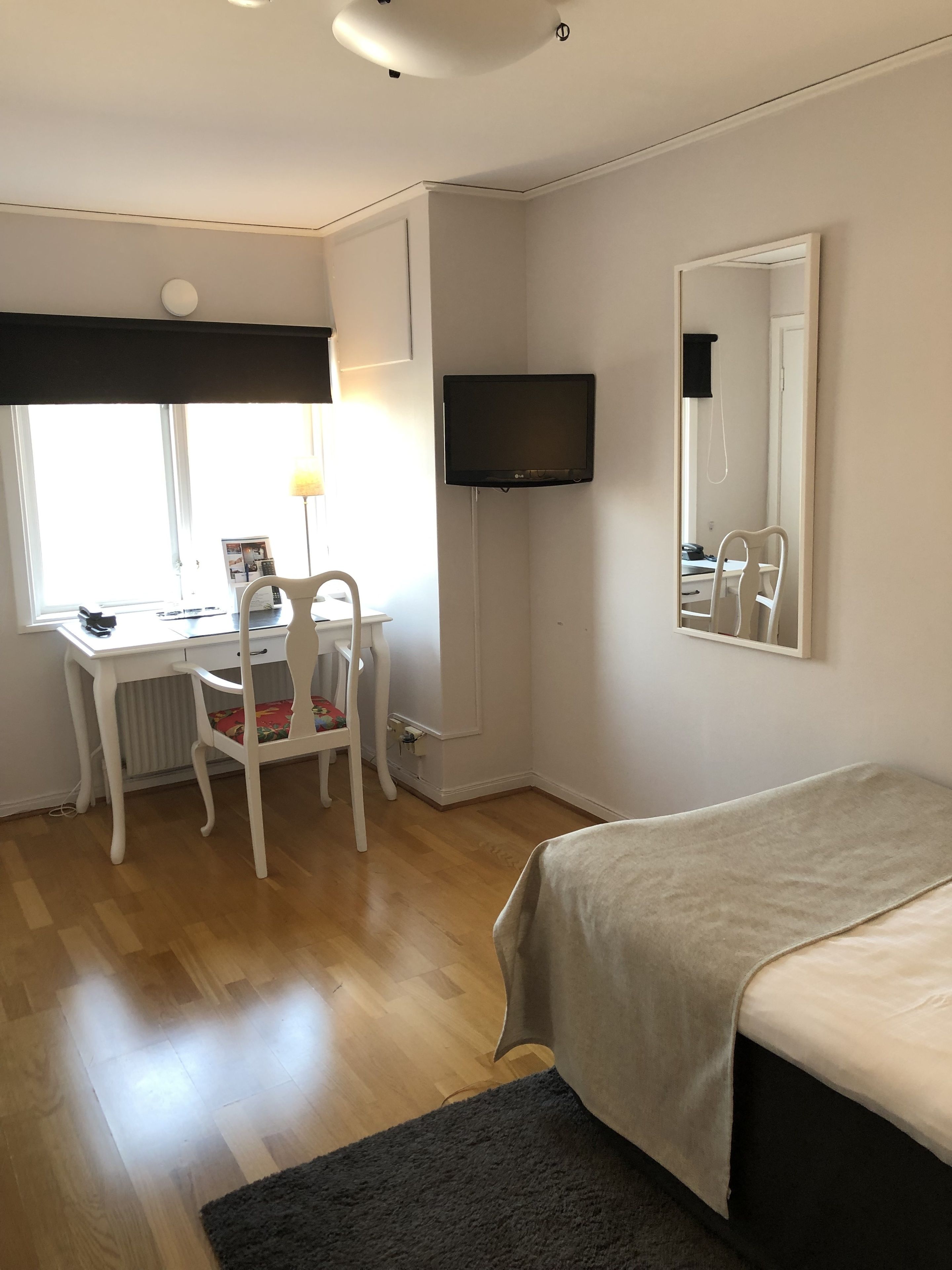 Une chambre à coucher avec un lit, un bureau et une chaise, un téléviseur fixé au mur et une fenêtre.