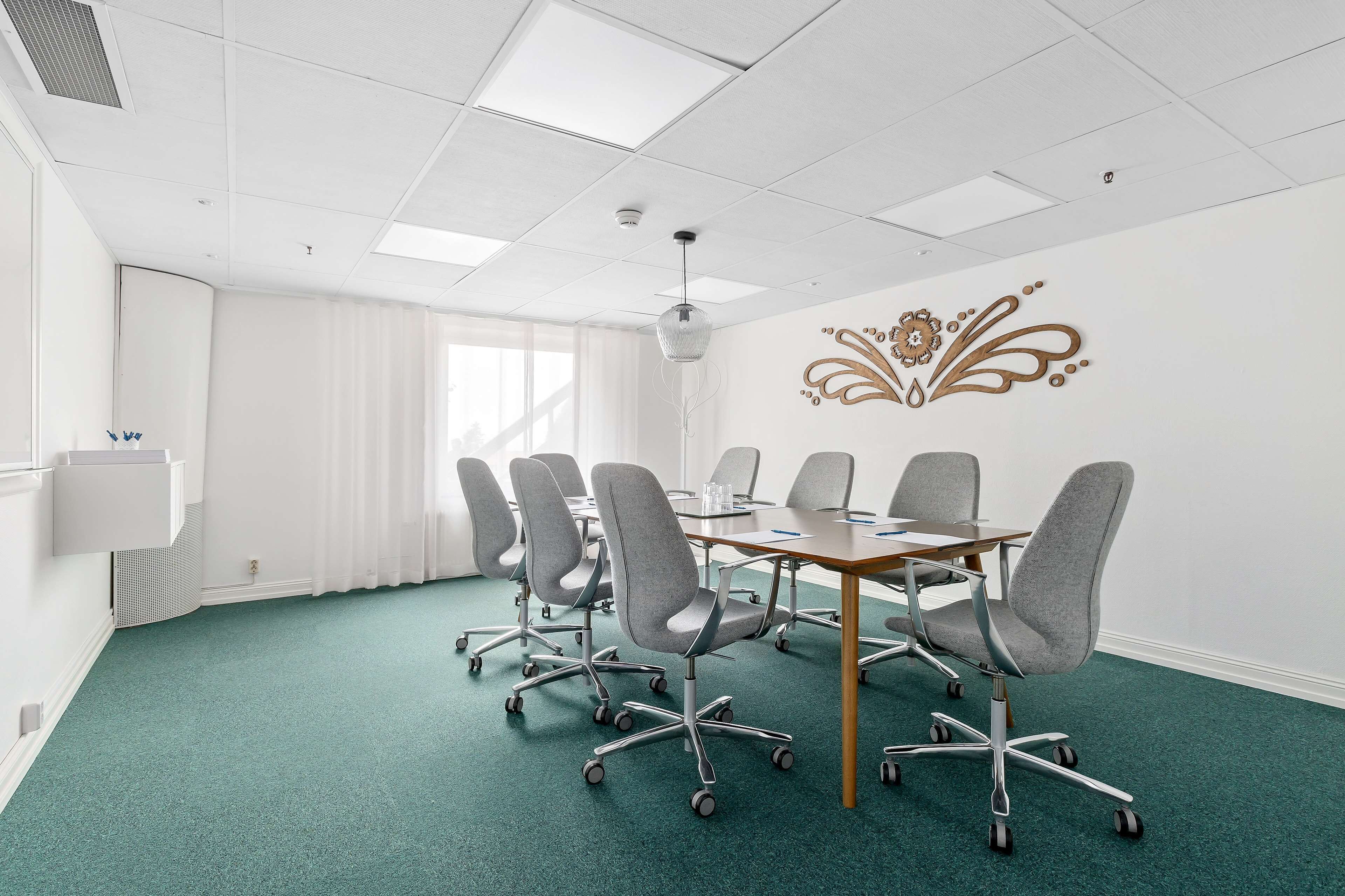 A conference room with a green carpet, white walls, and a decorative wall piece.