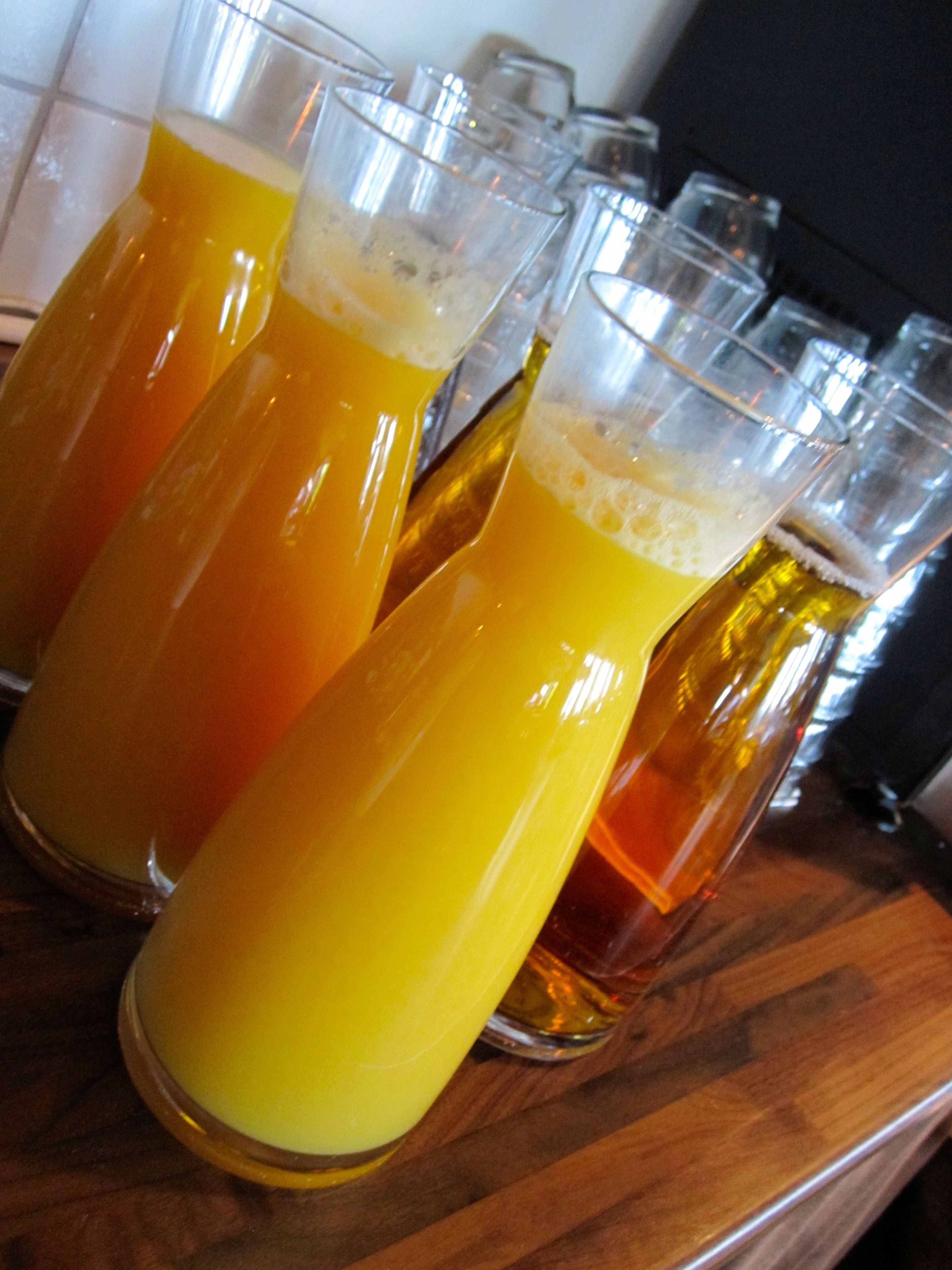 Une rangée de verres remplis d’une boisson jaune, probablement de la bière, posés sur une surface en bois.