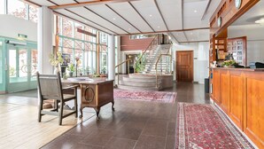 Un hall d’entrée spacieux avec un comptoir de réception en bois, un escalier et une grande fenêtre.