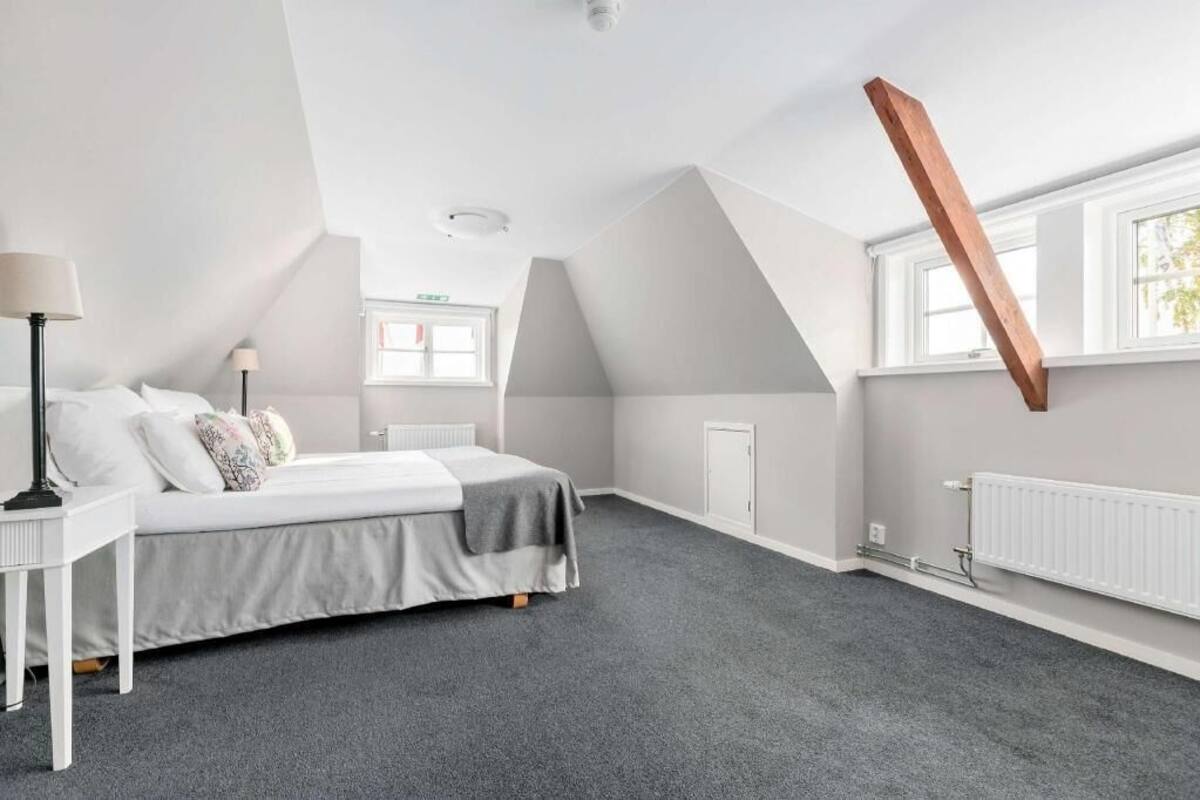 A bedroom with a sloped ceiling, a bed, a nightstand, a lamp, and a window.