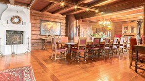 Une salle à manger spacieuse, avec des tables et des chaises en bois, une cheminée et un lustre.