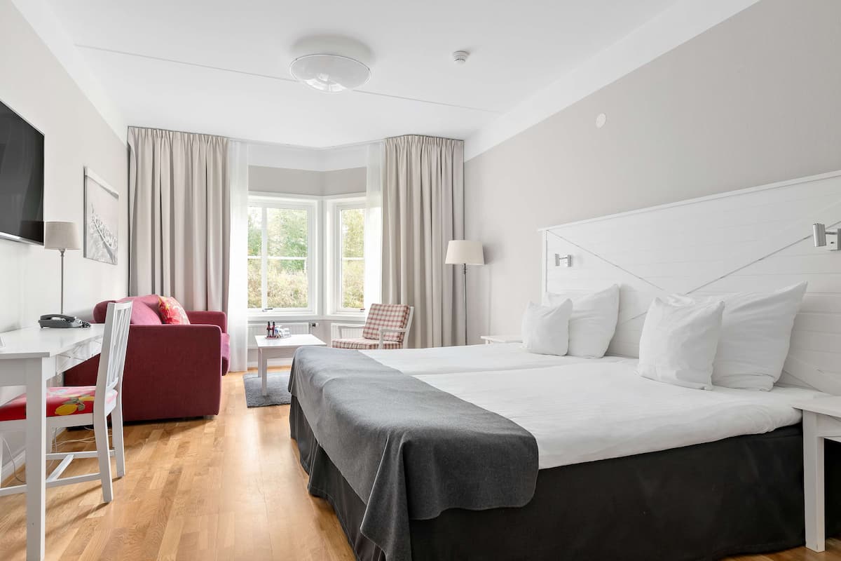 A hotel room with a large bed, a desk with a chair, a TV, and a window with curtains.