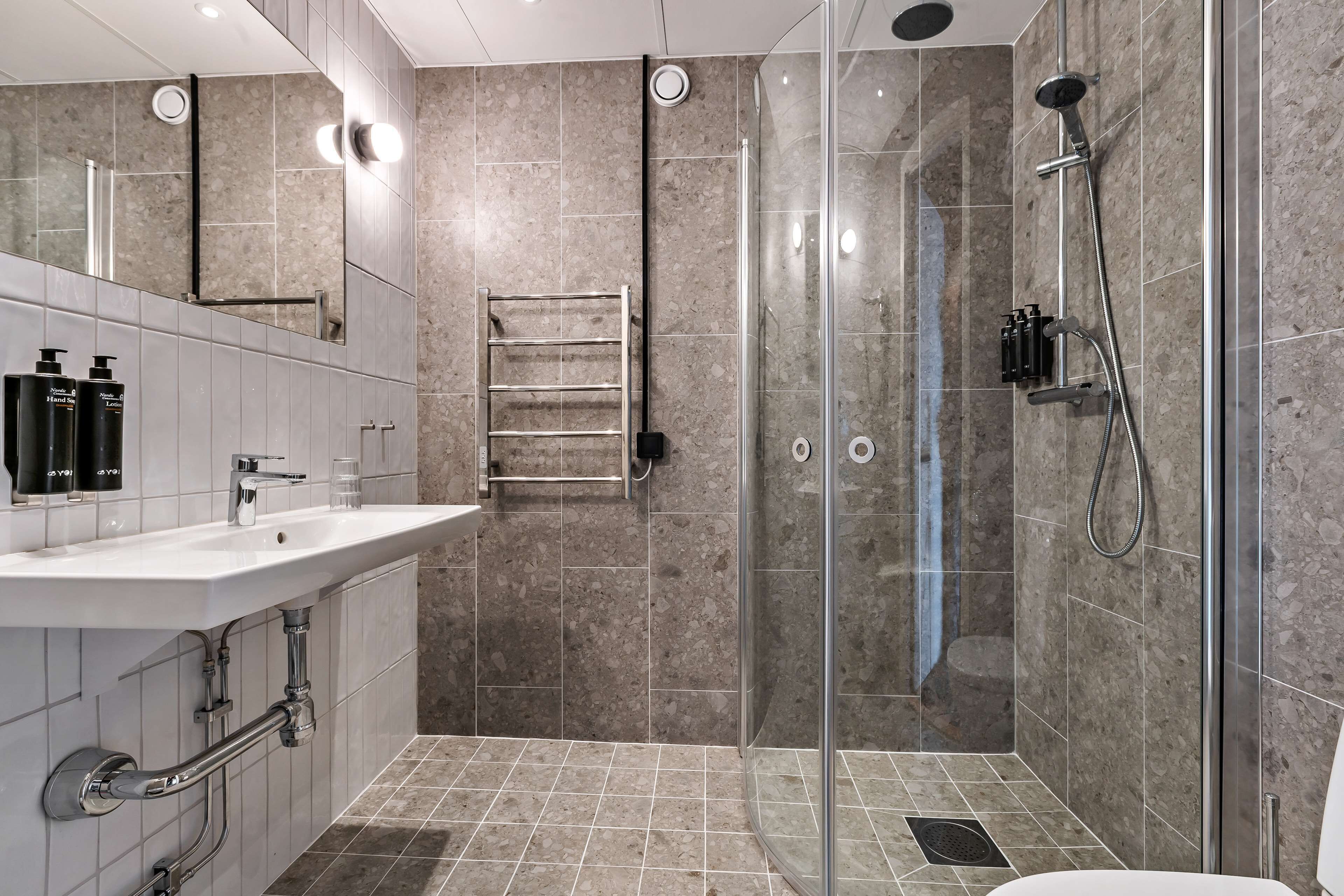 Une salle de bain moderne avec une douche à parois de verre, un lavabo blanc avec un miroir et un porte-serviettes.