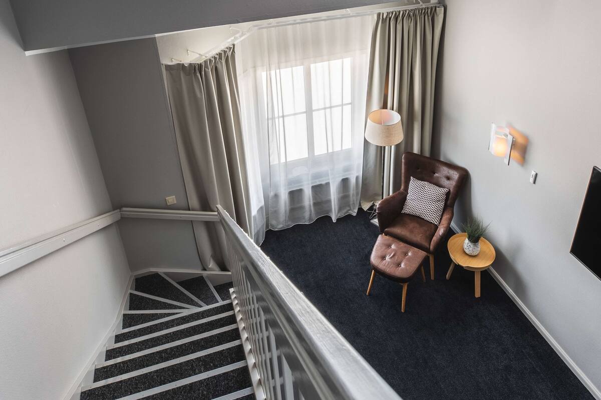 A staircase leading to a room with a chair, a small table with a plant, and a wall-mounted lamp.