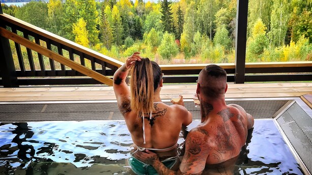 Deux personnes dans un jacuzzi, avec une vue magnifique sur les arbres et les montagnes.