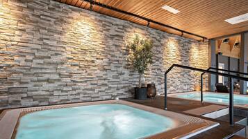 Un área de spa con dos jacuzzis, una pared de piedra, techo de madera y una escalera.