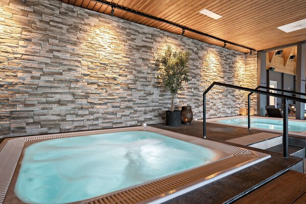 A spa area with two hot tubs, a stone wall, wooden ceiling, and a staircase.