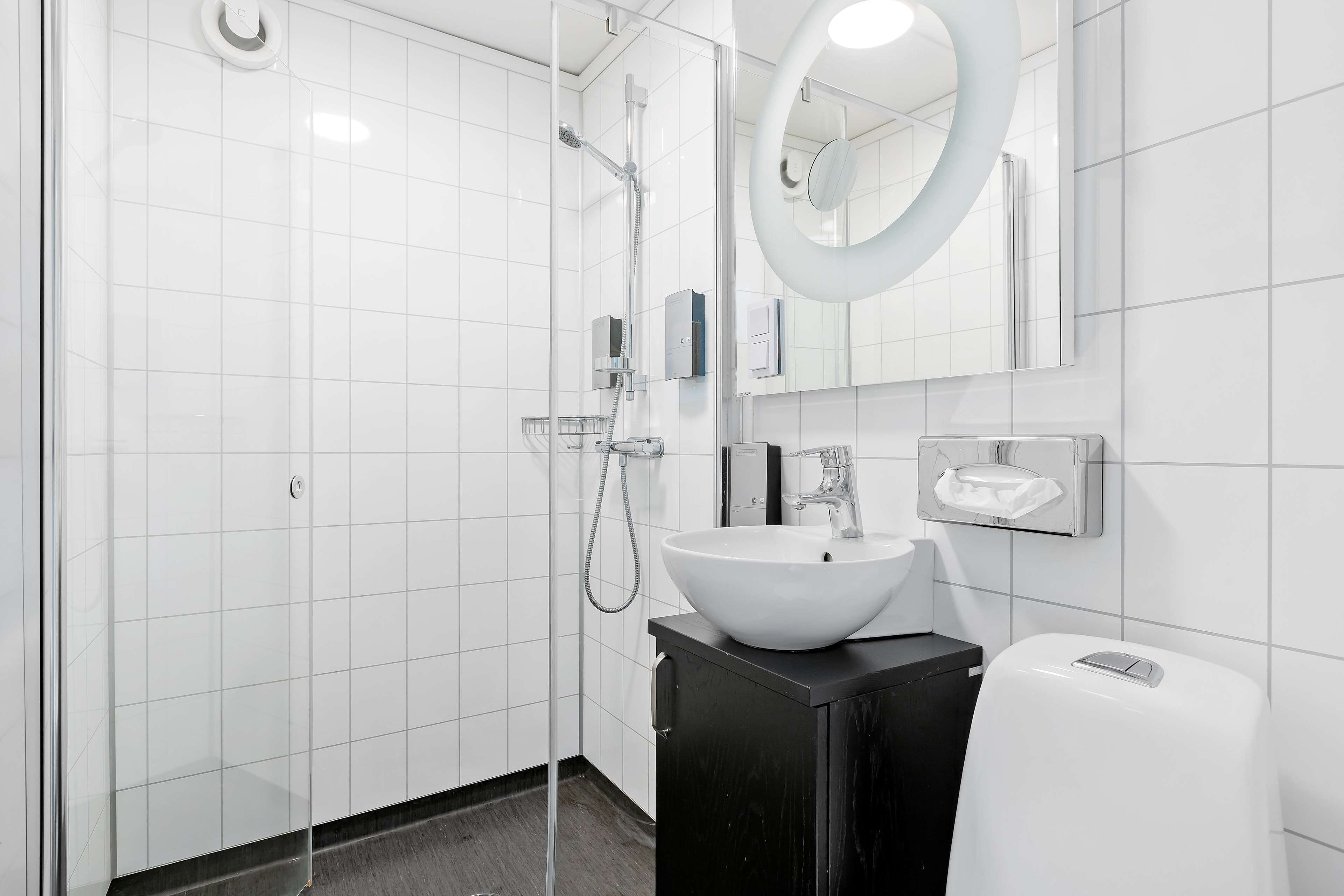 A modern bathroom with a glass-enclosed shower, a white sink, and a black vanity.