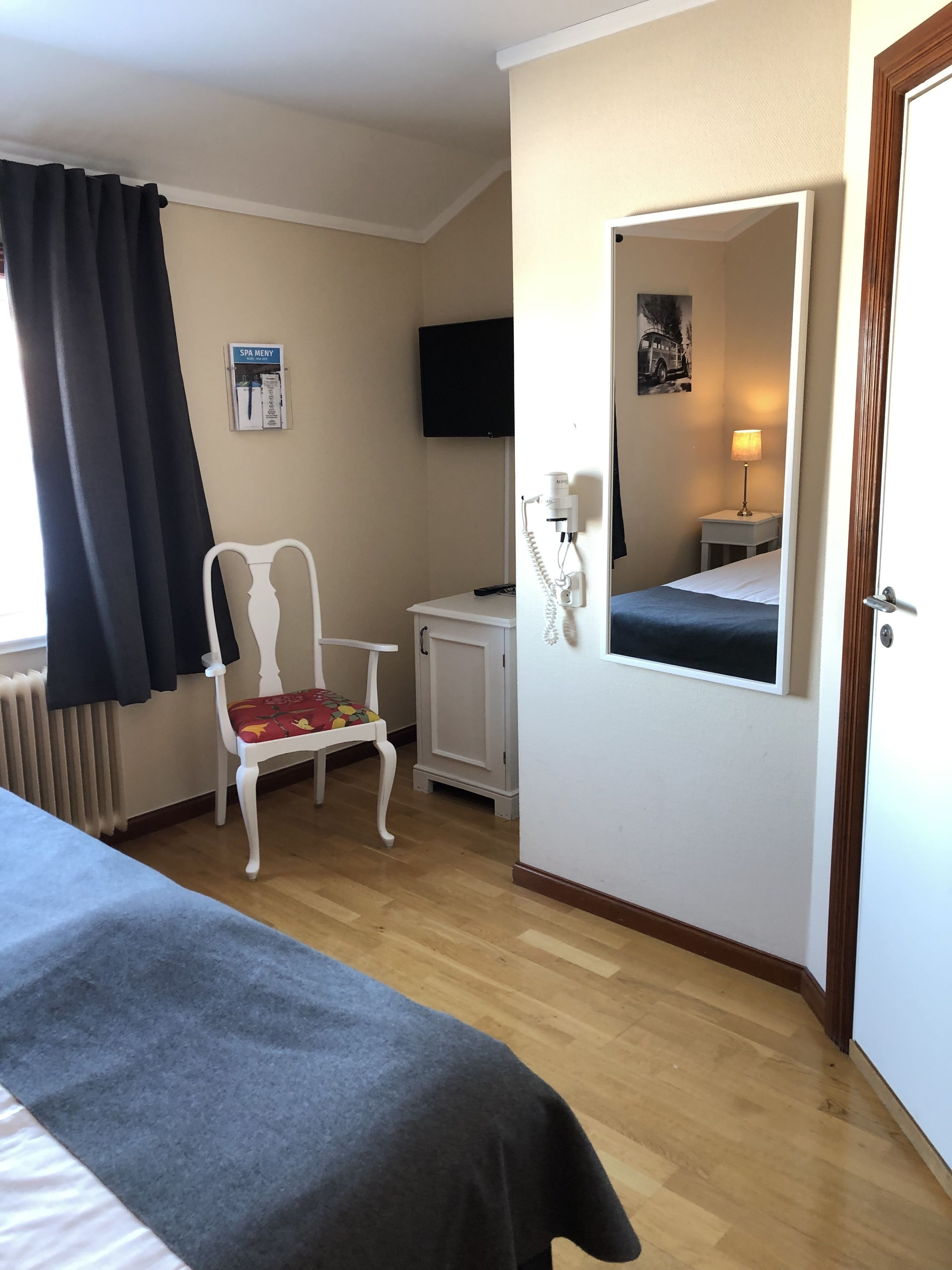 A hotel room with a bed, a chair, a small table, a mirror, a TV, and a spa menu sign.
