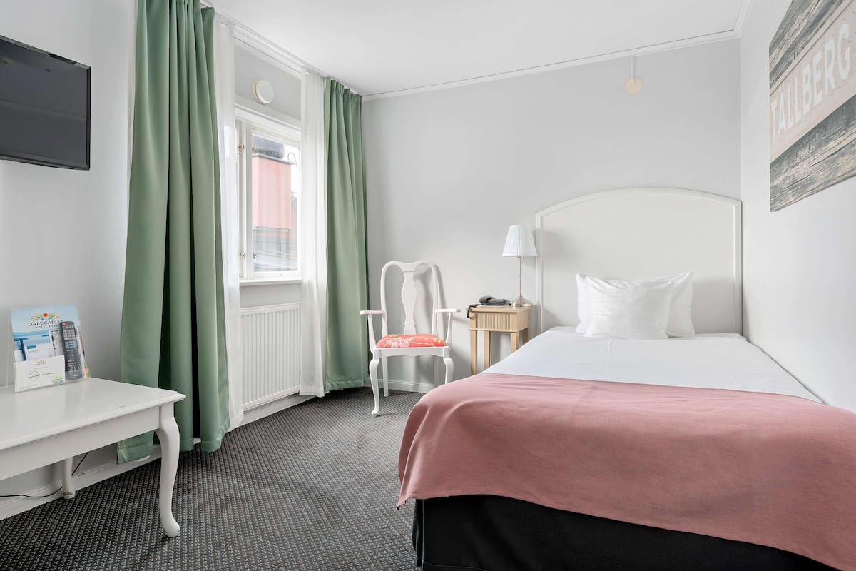 A hotel room with a bed, a desk, a chair, a lamp, and a window with curtains.