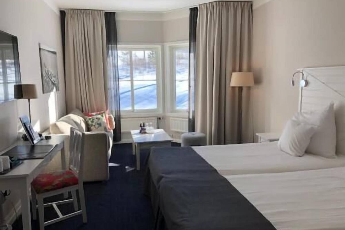 A hotel room with a bed, a desk, a chair, a lamp, and a window with curtains.