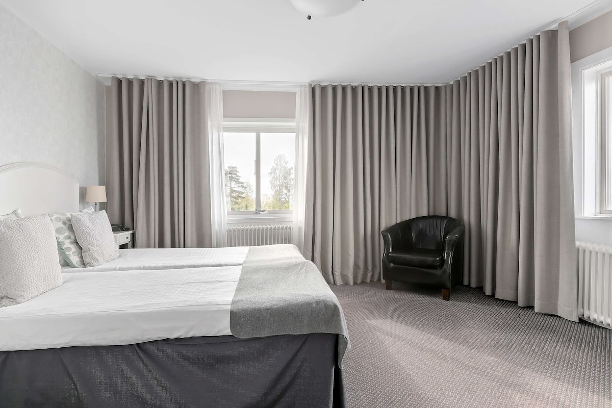A hotel room with a bed, a chair, and curtains.