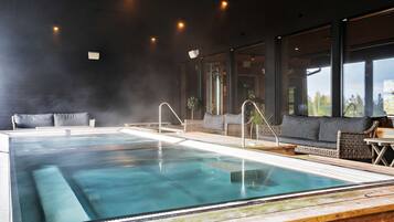 Un área de piscina interior moderna con agua cristalina, terraza de madera y asientos junto a la piscina.