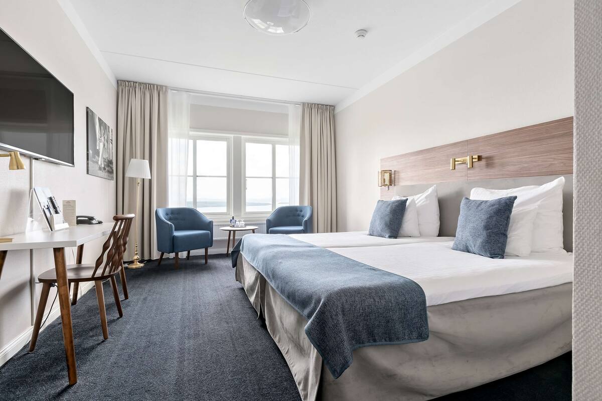 A hotel room with a large bed, a desk with a chair, a TV, and a window with curtains.
